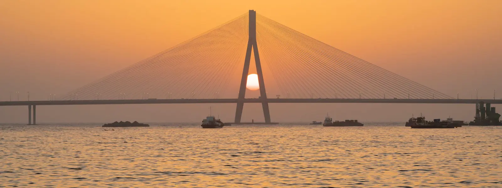 Bandra-Worli Sea Link cable-stayed bridge in Mumbai silhouetted against an orange sunset over the sea