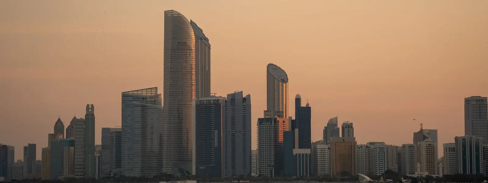Abu Dhabi Corniche skyline of modern towers across calm Gulf water at dusk
