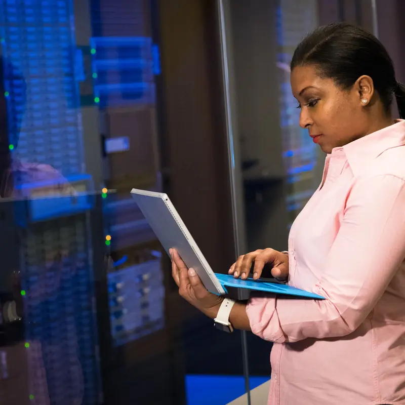 Engineer checking a laptop beside glass-fronted server cabinets inside a data hall