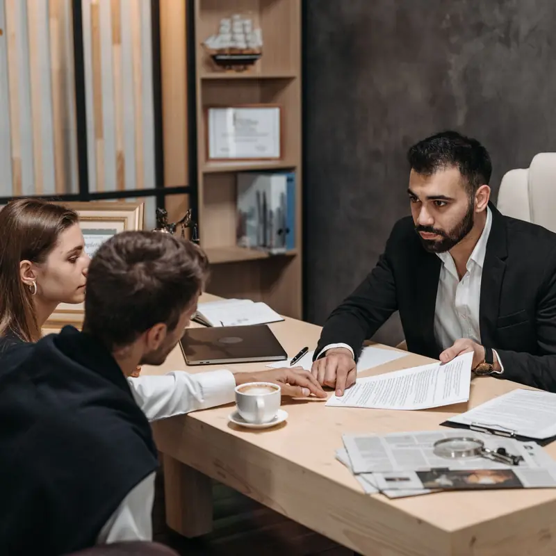 Advisor talking a client team through contract documents across a desk in a calm meeting