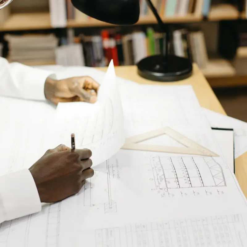 Analyst marking up construction drawings and project records at a desk during a review