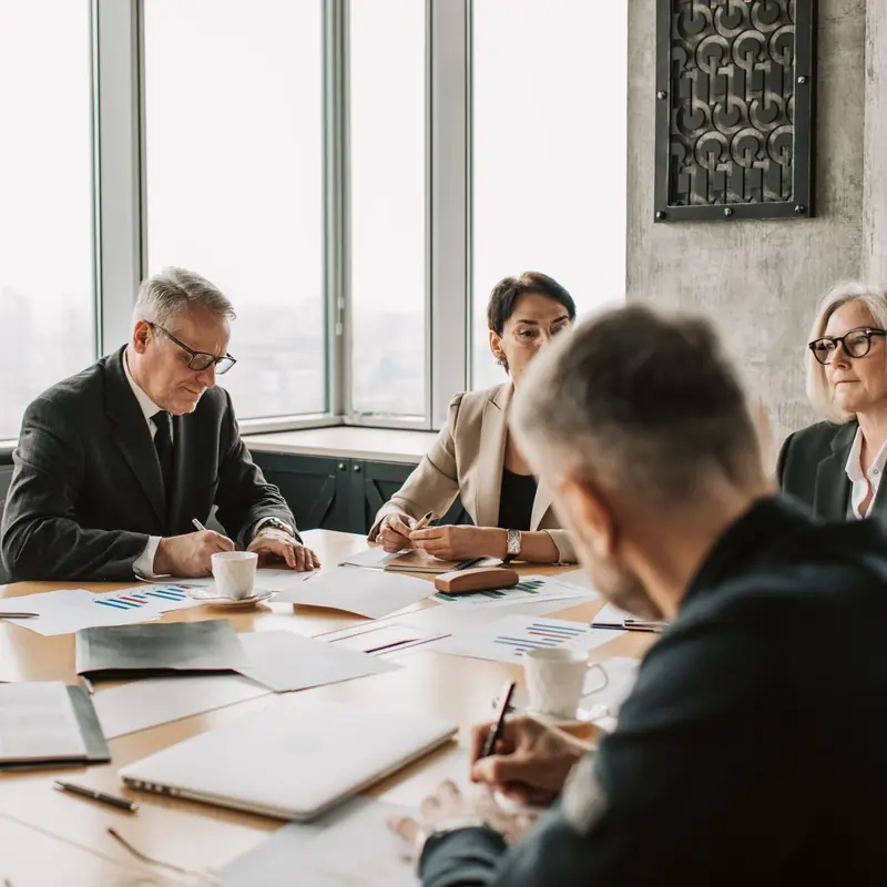 Senior leaders reviewing reports and charts around a boardroom table at a governance meeting